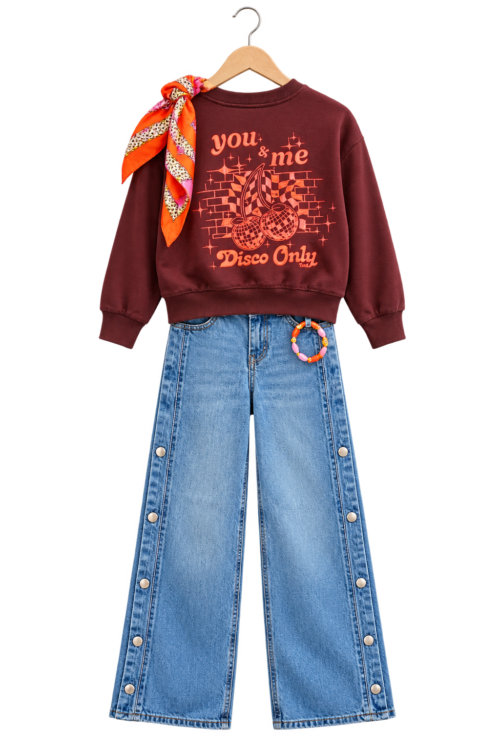 Disco cherry: Bordeaux sweater met vrolijke oranje kersenprint op de rug, jeans met drukknopen langs de zijkant, een kleurrijk sjaaltje en armband.